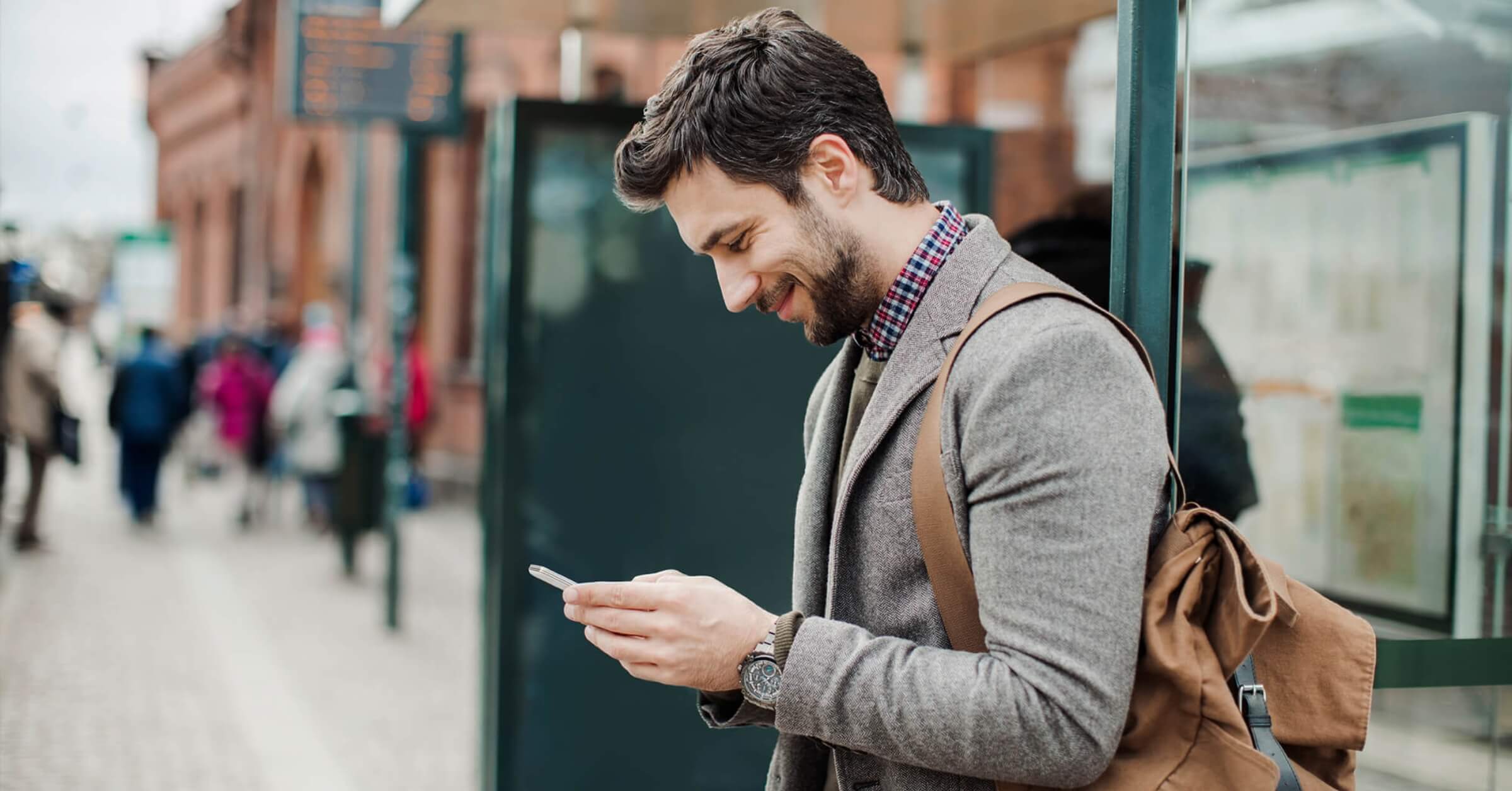 Ung mann på gata leser på telefonen og smiler